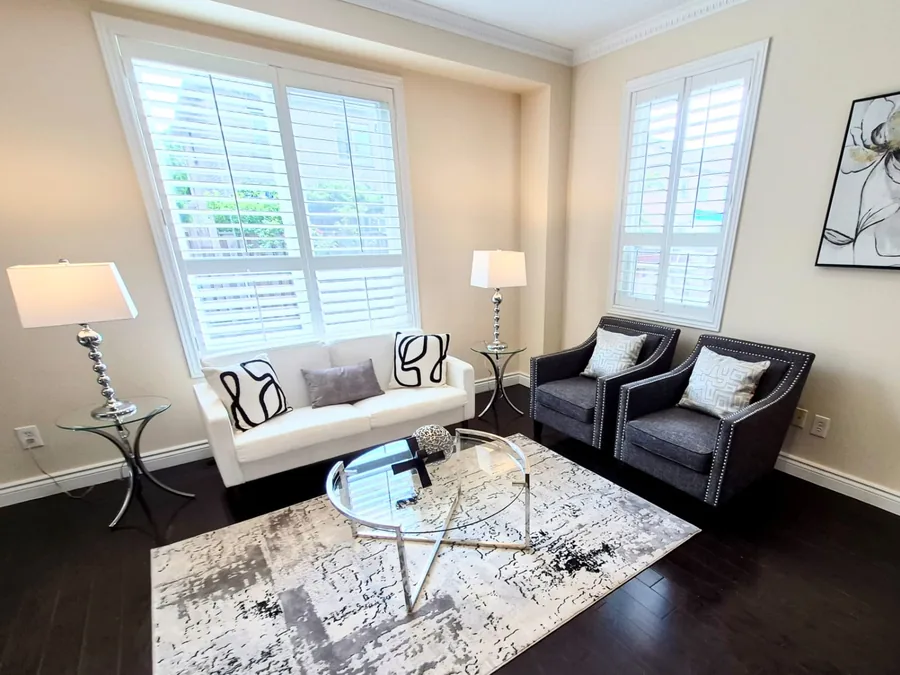 Bright sitting room with a white sofa, charcoal armchairs, and glass table
